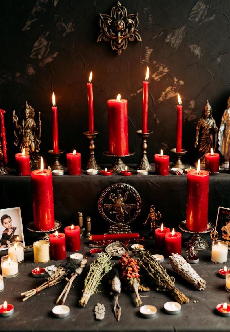 May include: A dark, moody scene featuring lit red candles of varying sizes, displayed on ornate candle holders. The arrangement includes small statues, dried herbs, and a decorative medallion, creating a mystical ambiance. The background is a dark, textured wall.
