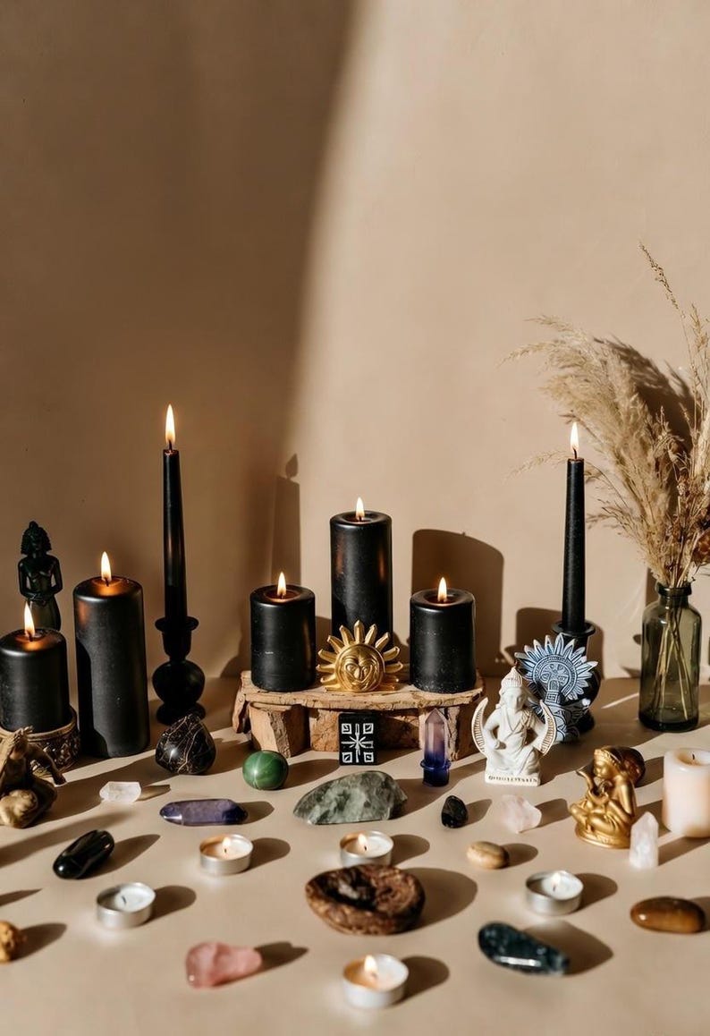 May include: An assortment of black candles, crystals, and decorative objects arranged on a beige surface. The candles vary in size and shape, some are lit. Other items include a sun-shaped ornament, small statues, and stones, creating a mystical theme.