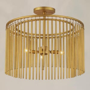 May include: A gold-colored, cylindrical ceiling light fixture. The light has a circular frame with vertical rods suspended from it, creating a cage-like design. Three light bulbs are visible inside the fixture, and it is mounted to a circular base.