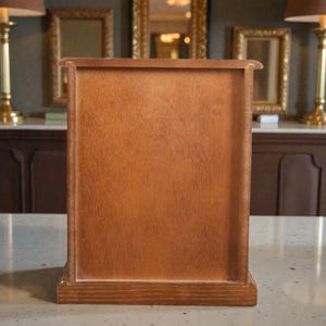 May include: A rectangular wooden cabinet with a light brown finish. The cabinet has a simple design with a flat front and a base. The wood grain is visible. The cabinet is likely for storage or display.