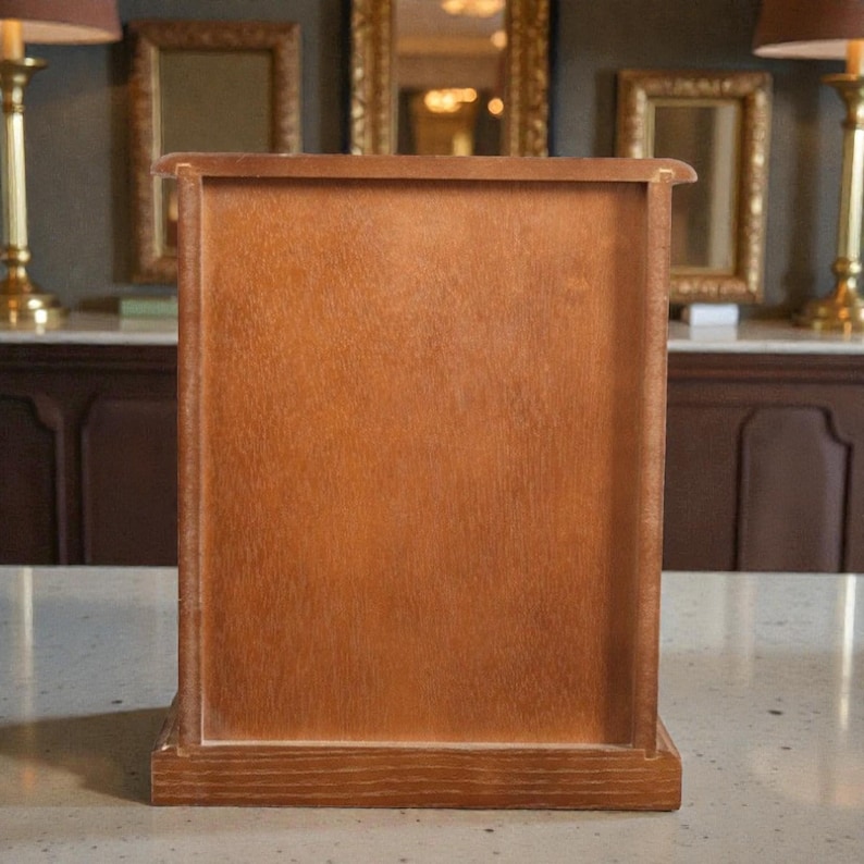 May include: A rectangular wooden cabinet with a light brown finish. The cabinet has a simple design with a flat front and a base. The wood grain is visible. The cabinet is likely for storage or display.