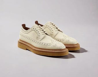 May include: A pair of cream-colored leather brogue shoes with decorative perforations and light brown soles. The shoes have a classic lace-up design and a sturdy, textured sole.