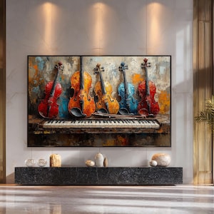 Op de afbeelding: Een abstract schilderij van vijf violen in rood, oranje en blauw, rustend op een pianoklavier. Het kunstwerk is zwart omlijst en hangt boven een donkergrijze stenen plank. De achtergrond heeft een textuur, kleurrijke uitstraling.