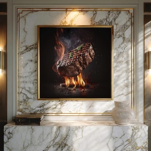 Op de afbeelding: Een ingelijst kunstwerk toont een gegrilde steak met vlammen en rook. De steak is gegarneerd met een takje rozemarijn. Het kunstwerk wordt tentoongesteld op een marmeren muur met gouden randen, en een decoratieve vaas staat op de marmeren plank eronder.