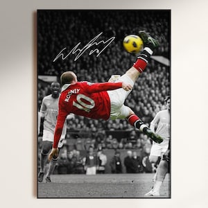 May include: A framed sports photograph featuring Wayne Rooney in a red jersey with the number 10 performing a bicycle kick. The background is in black and white, showing a stadium crowd and other players. A white signature is visible at the top.
