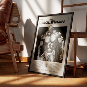 May include: Black framed poster featuring a black and white image of bodybuilder Ronnie Coleman. The poster has the name "RONNIE COLEMAN" at the top and additional text at the bottom. The poster is leaning against a wooden shelf and a brown leather chair.