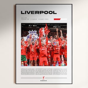 May include: A framed poster with the word "LIVERPOOL" at the top, and the text "24/25 PREMIER LEAGUE CHAMPIONS". The image shows a team in red uniforms celebrating with a trophy. The poster has a black frame.