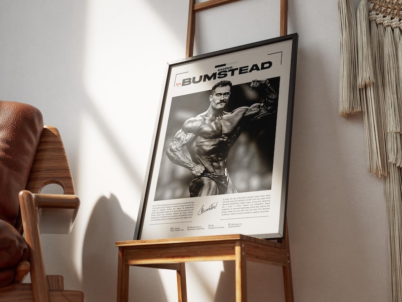 May include: Black and white framed poster featuring bodybuilder Chris Bumstead. The poster is displayed on a wooden stand. The poster includes the name "CHRIS BUMSTEAD" at the top and a signature at the bottom. The image is in a room with a wooden chair and a ladder.