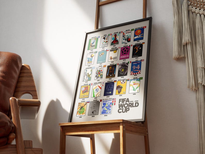 May include: Framed poster featuring FIFA World Cup logos from 1930 to 2026. The poster has a black frame and is displayed on a wooden table. The logos are arranged in a grid, each representing a different year and host country. The words "FIFA WORLD CUP" are printed in white.