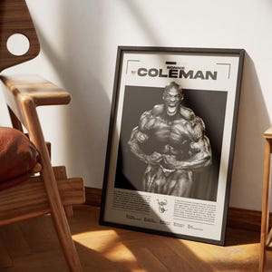 May include: A framed poster featuring a black and white image of bodybuilder Ronnie Coleman flexing his muscles. The poster has the name "RONNIE COLEMAN" at the top and a signature at the bottom. The poster is leaning against a wall.
