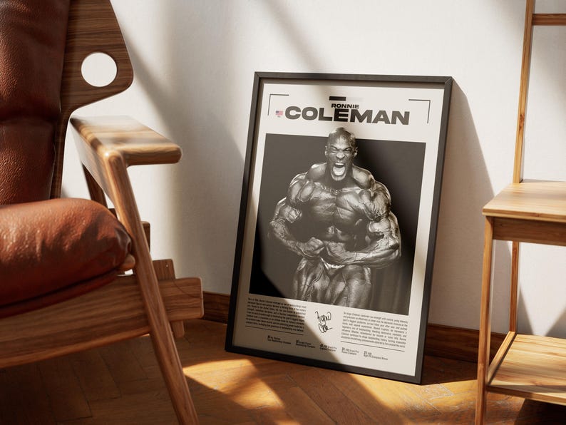 May include: A framed poster featuring a black and white image of bodybuilder Ronnie Coleman flexing his muscles. The poster has the name "RONNIE COLEMAN" at the top and a signature at the bottom. The poster is leaning against a wall.