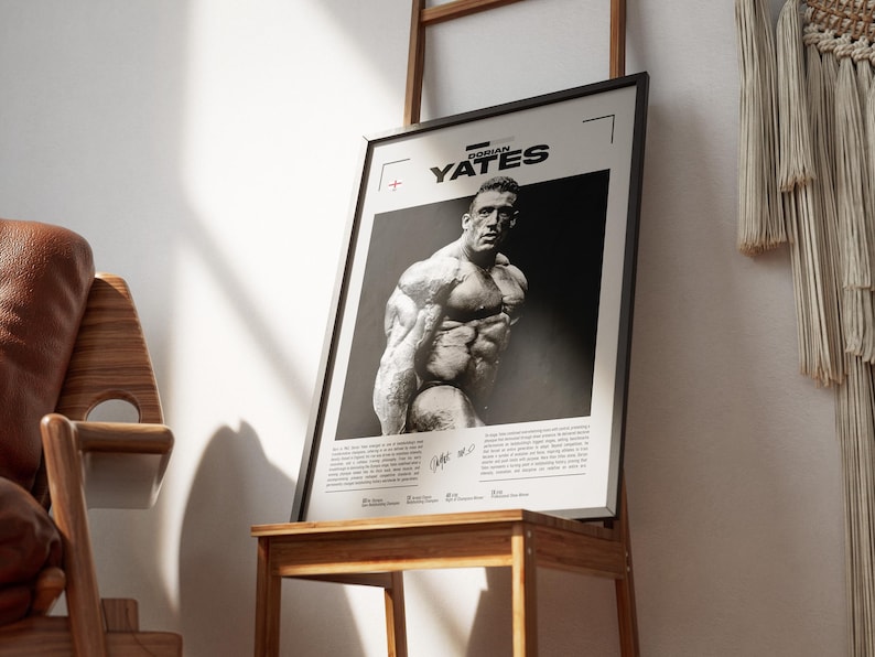 May include: Black and white framed poster featuring a bodybuilder. The poster has the name "Dorian Yates" at the top. The image is of a muscular man. The poster is displayed on a wooden stand.
