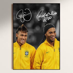 May include: A framed black and white photograph of two soccer players in yellow jackets. The image includes the signatures of the players, Neymar and Ronaldinho, above their heads. The jackets have the Brazilian flag and the word "Brasil".