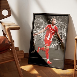 Pode incluir: Fotografia a preto e branco emoldurada de um jogador de futebol com uniforme vermelho e branco, em corrida, com uma assinatura. O jogador &eacute; o ponto focal, contra um fundo desfocado de um est&aacute;dio. A moldura &eacute; retangular.