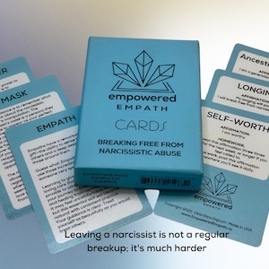 May include: A deck of "Empowered Empath Cards" in a light blue box, with the text "Breaking Free From Narcissistic Abuse." Several light blue cards are fanned out around the box, with affirmations and text. The text "Leaving a narcissist is not a regular breakup; it's much harder" is at the bottom.