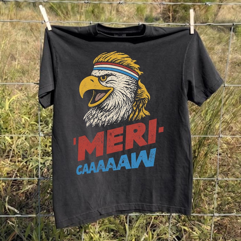 Distressed retro graphic featuring a bald eagle with a squawking open yellow beak and a blonde mullet haircut. The eagle wears a red, white, and blue striped athletic sweatband. Below the illustration, large weathered block text reads "'MERI-" in red, stacked above "CAAAAAW" in bright blue.