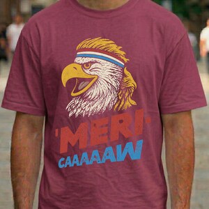 Distressed retro graphic featuring a bald eagle with a squawking open yellow beak and a blonde mullet haircut. The eagle wears a red, white, and blue striped athletic sweatband. Below the illustration, large weathered block text reads "'MERI-" in red, stacked above "CAAAAAW" in bright blue.