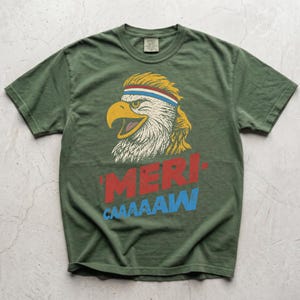 Distressed retro graphic featuring a bald eagle with a squawking open yellow beak and a blonde mullet haircut. The eagle wears a red, white, and blue striped athletic sweatband. Below the illustration, large weathered block text reads "'MERI-" in red, stacked above "CAAAAAW" in bright blue.