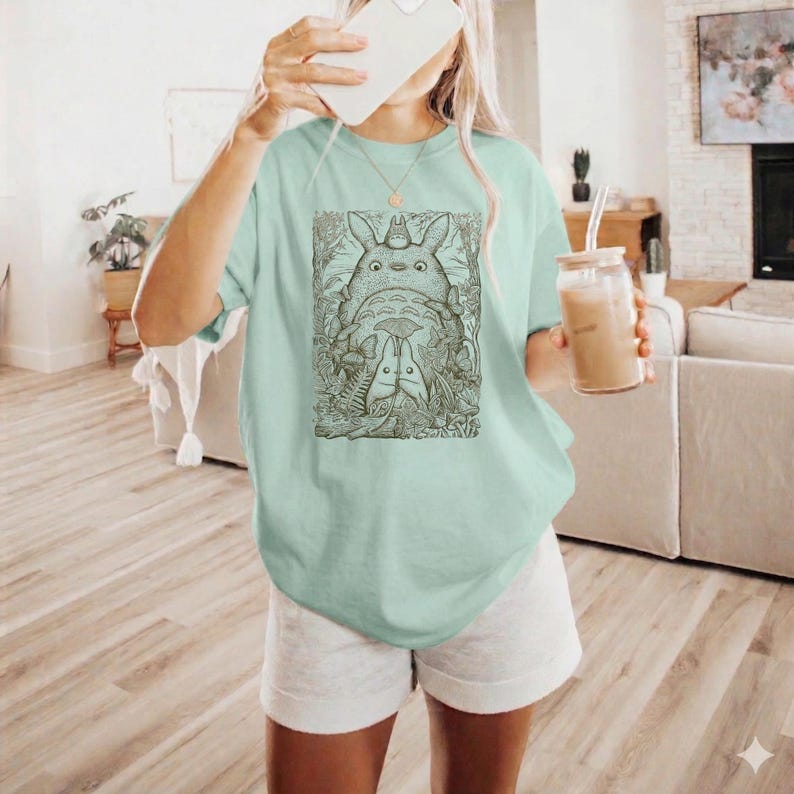 Pode incluir: Uma caneca de cer&acirc;mica branca com uma al&ccedil;a preta e o texto "But First, Coffee" em negrito preto. A caneca est&aacute; sobre um fundo desfocado, sugerindo um ambiente acolhedor.