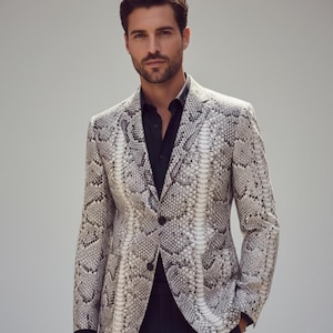 Może przedstawiać: Marynarka wężowa w odcieniach szarości i bieli. Marynarka ma zapięcie na dwa guziki i klapy z wycięciami. Osoba ma na sobie czarną koszulę. Ogólny styl jest modny i wyrafinowany.