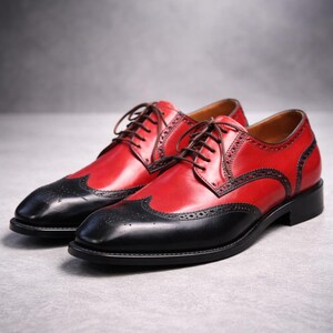 May include: A pair of red and black leather brogues with brown laces. The shoes feature a wingtip design with decorative perforations. The shoes are a classic formal style.