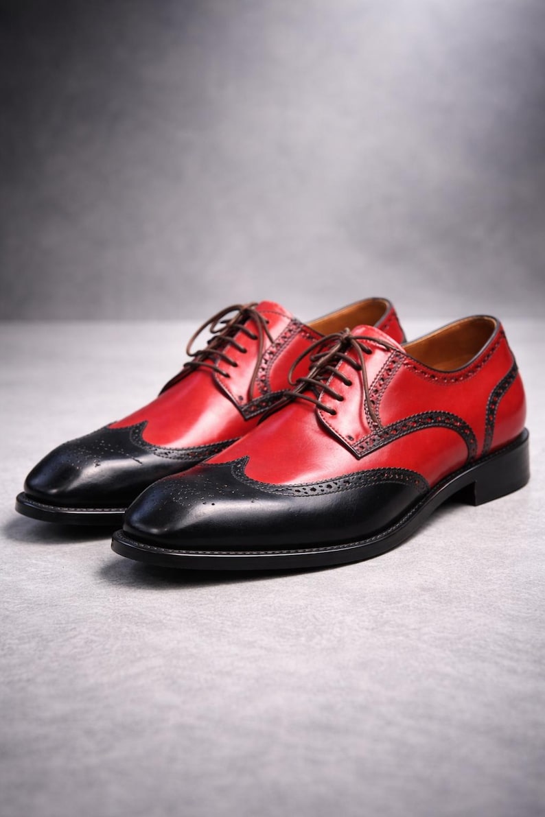 May include: A pair of red and black leather brogues with brown laces. The shoes feature a wingtip design with decorative perforations. The shoes are a classic formal style.