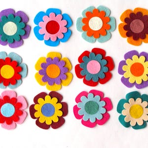 May include: A collection of twelve colorful felt flower embellishments. Each flower features layered petals in various colors like purple, blue, orange, and pink, with contrasting center circles. These craft supplies are ideal for DIY projects.