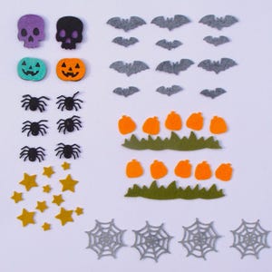 May include: A collection of Halloween-themed felt cutouts. Includes purple and black skulls, green and orange jack-o'-lanterns, gray bats, orange pumpkins, green grass, yellow stars, and gray spiderwebs. Perfect for crafting.