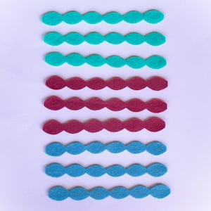 May include: Rows of felt shapes in teal, burgundy, and blue arranged vertically against a white background. Each row consists of connected, oval-shaped pieces, creating a scalloped edge. The felt appears to be a soft, craft material.