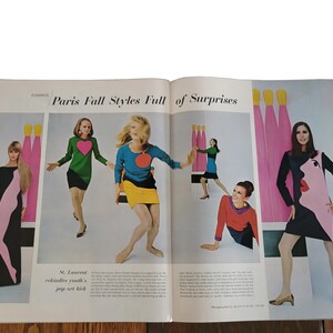 Op de afbeelding: Een magazine spread met modemodellen die kleurrijke jurken dragen met geometrische patronen. De tekst "Paris Fall Styles Full of Surprises" staat bovenaan de pagina. De modellen poseren tegen een achtergrond van abstracte vormen en kleuren.