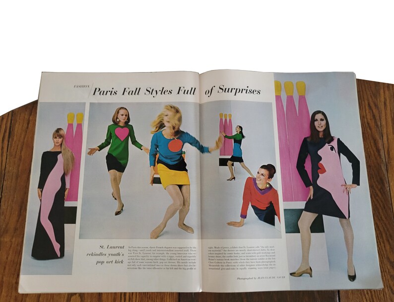 Op de afbeelding: Een magazine spread met modemodellen die kleurrijke jurken dragen met geometrische patronen. De tekst "Paris Fall Styles Full of Surprises" staat bovenaan de pagina. De modellen poseren tegen een achtergrond van abstracte vormen en kleuren.