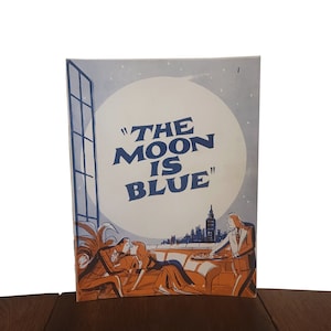 May include: A vintage playbill for the play "The Moon is Blue" featuring a scene of a couple on a rooftop overlooking a city skyline with a large moon in the background.