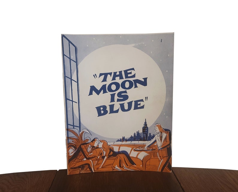 May include: A vintage playbill for the play "The Moon is Blue" featuring a scene of a couple on a rooftop overlooking a city skyline with a large moon in the background.