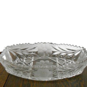 May include: A clear glass serving dish with a scalloped edge and intricate etched floral designs. The dish is oval shaped and has a raised center section.