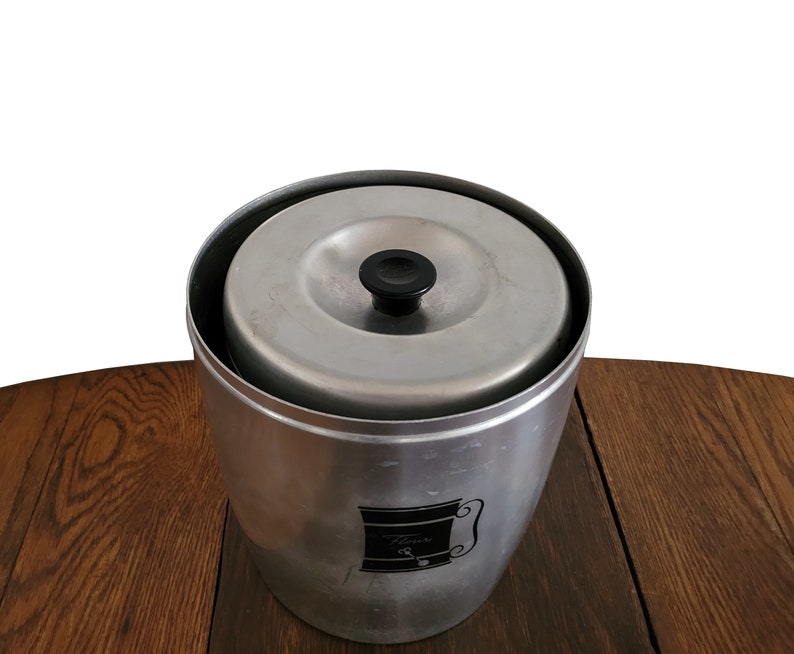 Puede incluir: Un recipiente de aluminio plateado con una perilla negra en la tapa. El recipiente tiene una etiqueta en blanco y negro con la palabra "Flavor" en ella.