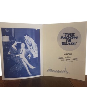 May include: A black and white photo of a playbill for the comedy "The Moon is Blue" by F. Hugh Herbert. The playbill features the names of the actors: Seward Andrews, Jacqueline Bolt, and Michael Lipton. The playbill is set against a backdrop of a city skyline.