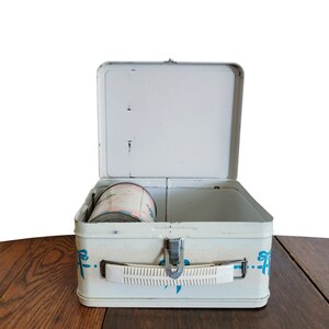 Peut inclure: Une bo&icirc;te &agrave; lunch en m&eacute;tal blanc avec des motifs de rubans bleus. La bo&icirc;te &agrave; lunch est ouverte et un petit r&eacute;cipient rose et blanc est &agrave; l'int&eacute;rieur.