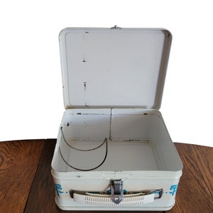 Peut inclure: Bo&icirc;te &agrave; lunch en m&eacute;tal blanc avec un motif bleu et blanc. La bo&icirc;te &agrave; lunch est ouverte et l'int&eacute;rieur est vide. Il y a une poign&eacute;e en m&eacute;tal sur le c&ocirc;t&eacute; de la bo&icirc;te &agrave; lunch.