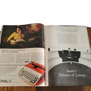 Op de afbeelding: Een dubbele pagina uit een vintage tijdschrift met een advertentie voor een Royal Portable typemachine. De advertentie toont een vrouw die aan een bureau werkt met boeken en een lamp. De typemachine is rood en wit en heeft de tekst "Help haar dit jaar georganiseerd te zijn met een Royal Portable." De andere pagina toont een zwart-witfoto van een man die op een gebogen platform zit met de tekst "Close-up: Fukio Mishima, een genie dat een legende bouwt." De tekst "Japans Dynamo van Letters" is ook te zien.