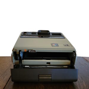 May include: A vintage Polaroid camera with a gray and black exterior. The camera is open, revealing the film compartment and a pull tab labeled "PULL".