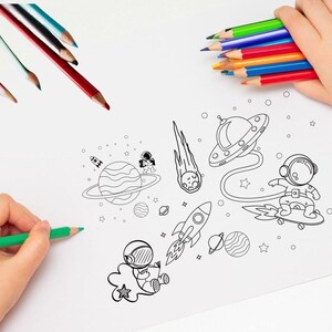 Può includere: Mani di un bambino che tengono matite colorate e disegnano un'immagine a tema spazio. Il disegno presenta pianeti, razzi, astronauti e un UFO. Le matite sono di vari colori.