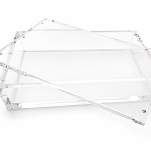 Puede incluir: Una bandeja rectangular transparente de acr&iacute;lico con una tapa separada. La bandeja presenta paredes gruesas y transparentes con una base plana, mientras que la tapa a juego descansa en &aacute;ngulo sobre la parte superior, fijada con tornillos met&aacute;licos.