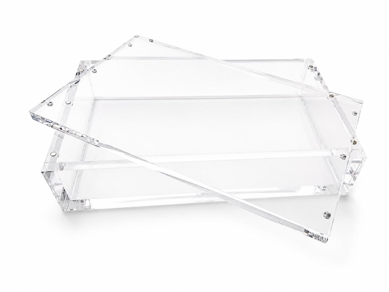 Puede incluir: Una bandeja rectangular transparente de acr&iacute;lico con una tapa separada. La bandeja presenta paredes gruesas y transparentes con una base plana, mientras que la tapa a juego descansa en &aacute;ngulo sobre la parte superior, fijada con tornillos met&aacute;licos.