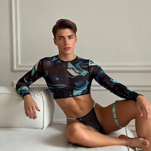 May include: Black mesh long-sleeve crop top and matching underwear set with a blue and teal abstract design. The set includes a garter belt with a light green band. The clothing is sheer and form-fitting.