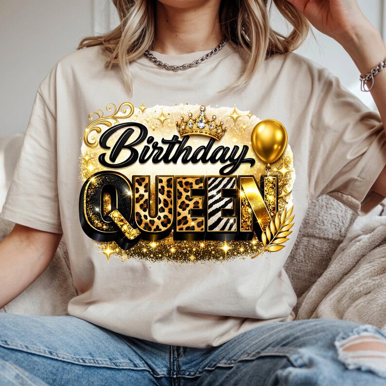 May include: A beige t-shirt featuring a graphic that reads "Birthday QUEEN" in black, gold, and leopard print. The design includes a gold crown, balloon, and laurel leaves. The shirt is made of a soft material.