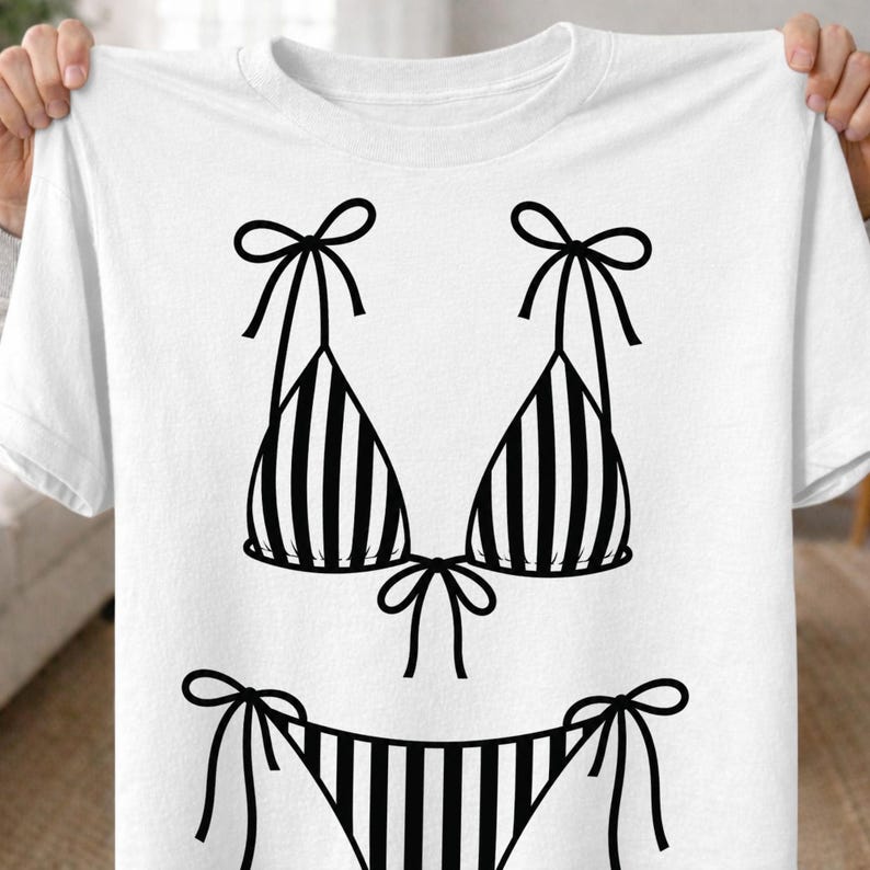 K&ouml;nnte beinhalten: Wei&szlig;es T-Shirt mit einem schwarz-wei&szlig; gestreiften Bikini-Design. Das Bikini-Oberteil hat Schleifen-Tr&auml;ger, und die Unterseite hat Schleifenverschl&uuml;sse an den Seiten. Das Design ist eine einfache, grafische Illustration.
