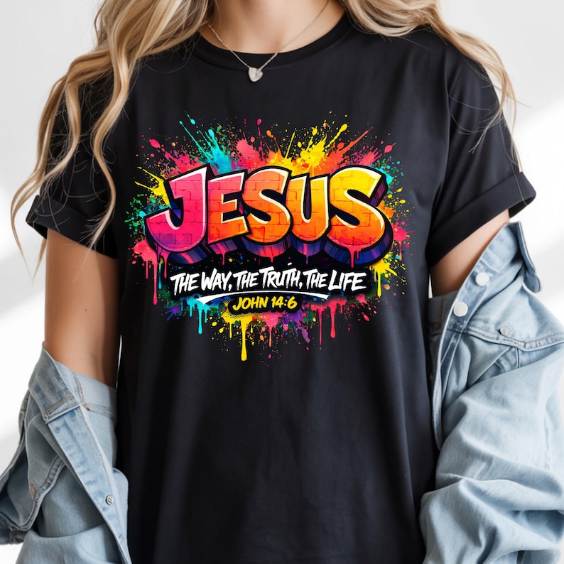 May include: Black t-shirt with a colorful graphic design. The design features the word "JESUS" in bold, outlined letters, with the text "THE WAY, THE TRUTH, THE LIFE" and "JOHN 14:6" below. The design has a graffiti-style aesthetic with paint splatters.