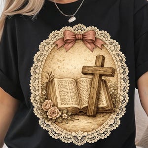 May include: Black t-shirt with a sepia-toned graphic. The design includes a wooden cross, an open book, and roses, all within an oval frame with a lace border and a bow. The overall aesthetic is vintage and detailed.
