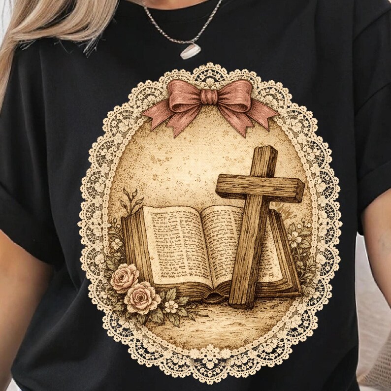 May include: Black t-shirt with a sepia-toned graphic. The design includes a wooden cross, an open book, and roses, all within an oval frame with a lace border and a bow. The overall aesthetic is vintage and detailed.