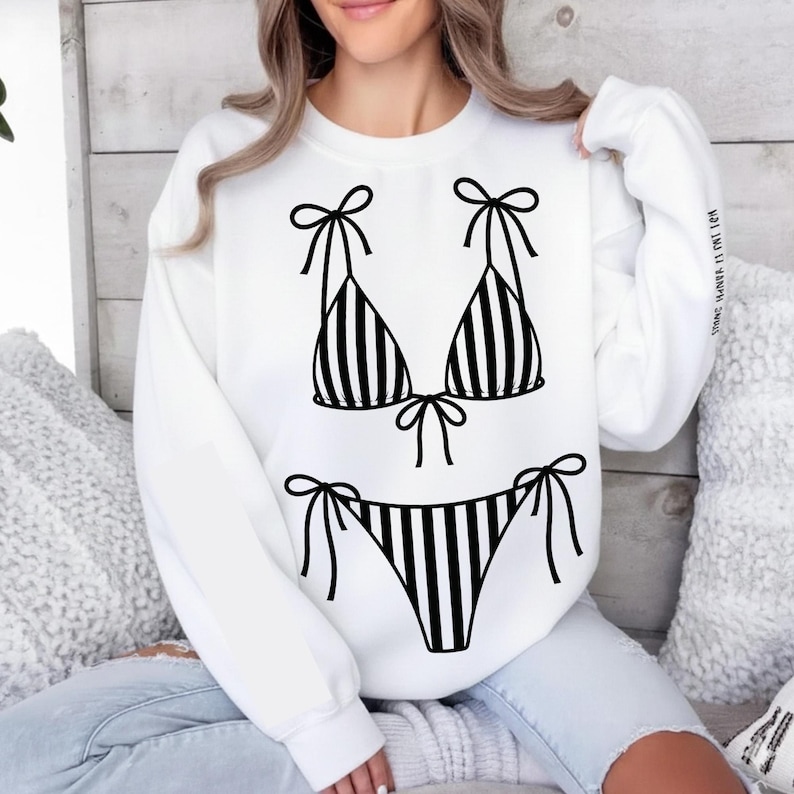 K&ouml;nnte beinhalten: Wei&szlig;es Sweatshirt mit einem schwarz-wei&szlig; gestreiften Bikini-Design. Das Bikini-Oberteil und -Unterteil sind mit Schleifendetails versehen. Ein l&auml;ssiges Kleidungsst&uuml;ck, geeignet f&uuml;r den Alltag.